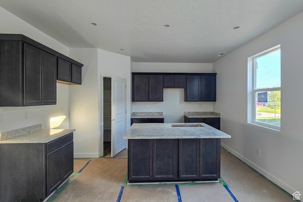 kitchen with baseboards, a kitchen island, light stone counters, and concrete floors