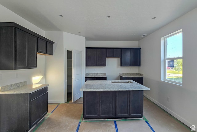 kitchen with baseboards, a kitchen island, light stone counters, and concrete floors