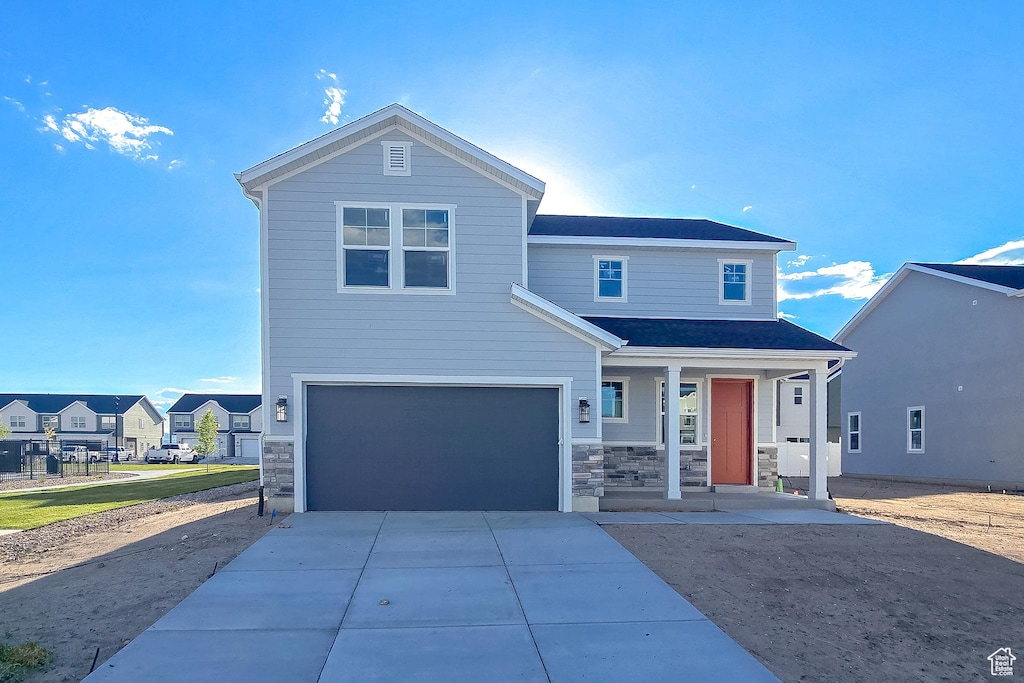 view of front of property with covered porch, an attached garage, driveway, and stone siding