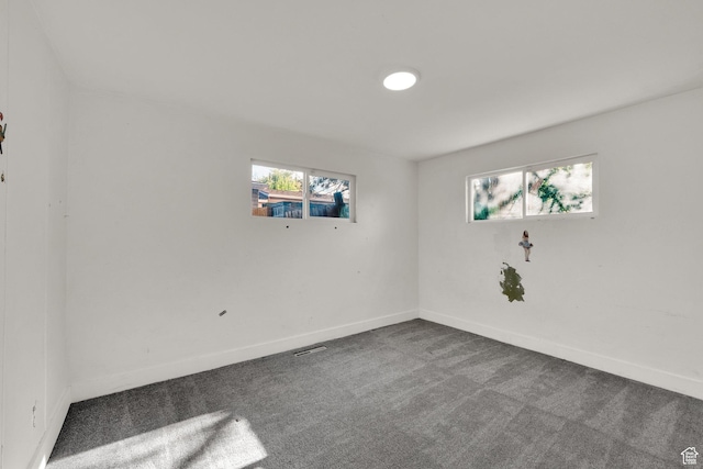 spare room featuring dark carpet and baseboards