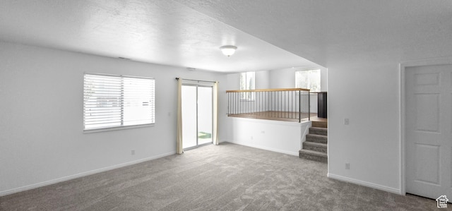 unfurnished living room with carpet floors, baseboards, a textured ceiling, and stairway
