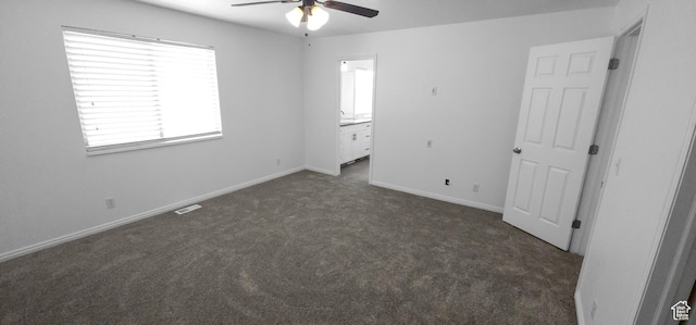 unfurnished bedroom with dark carpet, ensuite bath, baseboards, and ceiling fan