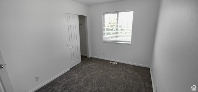 unfurnished bedroom featuring dark carpet, baseboards, and a closet