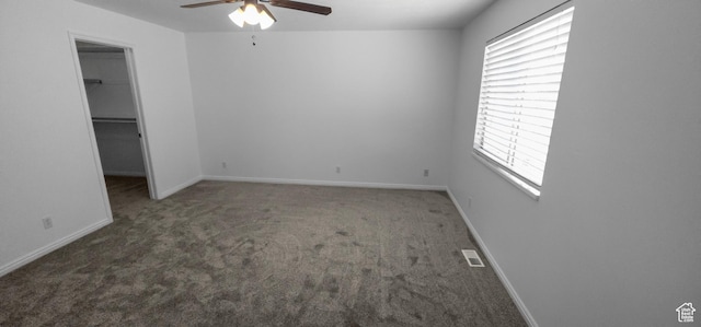 unfurnished bedroom with a walk in closet, carpet floors, baseboards, a closet, and a ceiling fan
