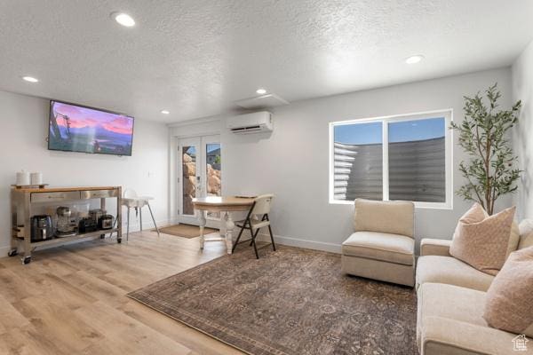 living room featuring an AC wall unit, recessed lighting, baseboards, wood finished floors, and a textured ceiling