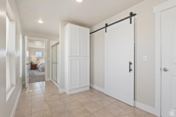 corridor featuring a barn door, baseboards, light tile patterned flooring, and recessed lighting