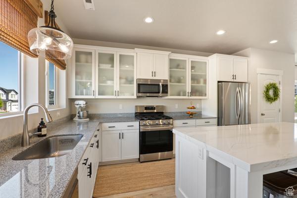 kitchen with appliances with stainless steel finishes, a sink, pendant lighting, light stone countertops, and white cabinets