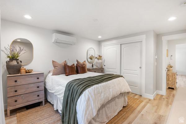 bedroom featuring an AC wall unit, light wood-style flooring, a closet, recessed lighting, and baseboards