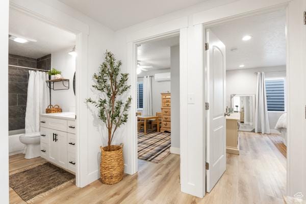 ensuite bathroom featuring a wall unit AC, wood finished floors, vanity, and shower / bathtub combination with curtain