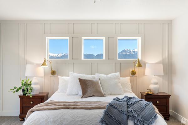 bedroom featuring baseboards, a decorative wall, multiple windows, and light carpet