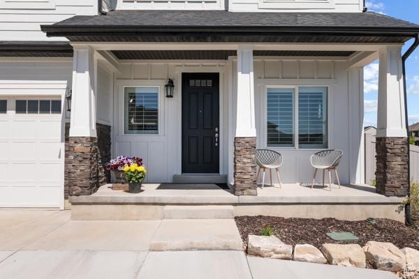 view of exterior entry featuring covered porch, board and batten siding, stone siding, and roof with shingles
