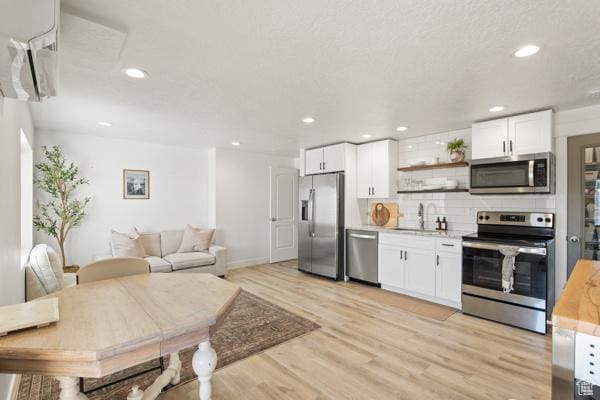 kitchen with appliances with stainless steel finishes, a sink, light wood-style flooring, open shelves, and white cabinetry