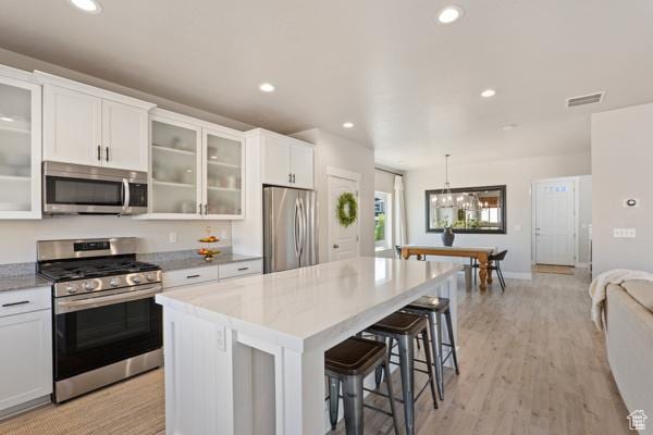 kitchen featuring stainless steel appliances, a kitchen island, white cabinetry, a breakfast bar area, and hanging light fixtures