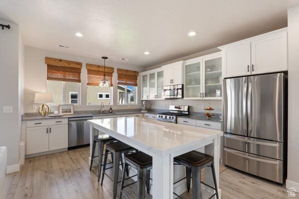 kitchen with stainless steel appliances, a sink, light wood finished floors, white cabinets, and a kitchen bar