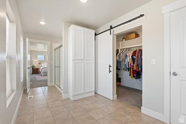 unfurnished bedroom with a barn door, a walk in closet, light tile patterned floors, a closet, and recessed lighting