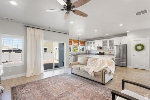 living area with ceiling fan, baseboards, recessed lighting, and light wood finished floors
