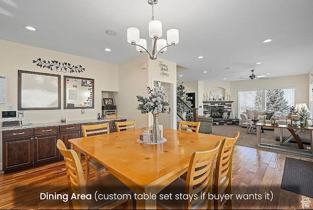 dining room featuring dark wood-type flooring, a glass covered fireplace, ceiling fan, recessed lighting, and a chandelier