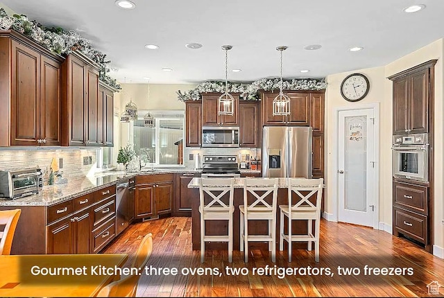 kitchen with appliances with stainless steel finishes, a sink, a kitchen breakfast bar, a center island, and dark wood-type flooring