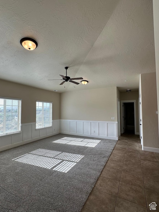 unfurnished room featuring a textured ceiling, ceiling fan, wainscoting, and tile patterned flooring
