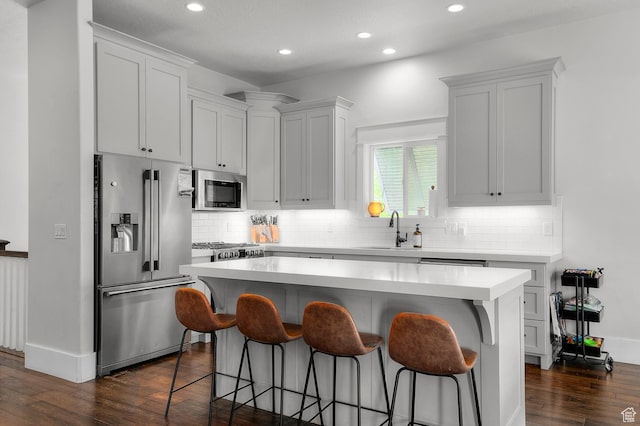 kitchen with appliances with stainless steel finishes, a sink, a breakfast bar, a center island, and dark wood-style floors