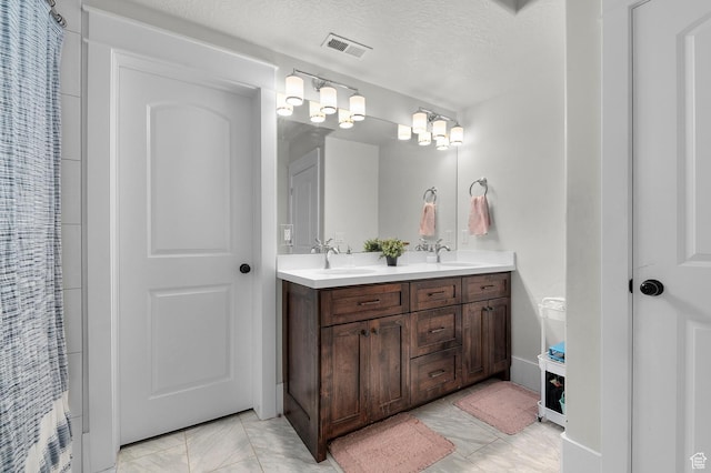 full bathroom featuring double vanity, a textured ceiling, and marble finish floors