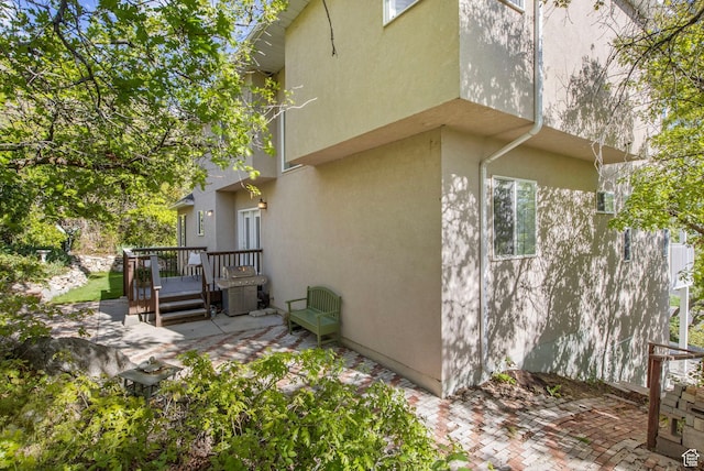view of side of home featuring a patio area, a wooden deck, and stucco siding
