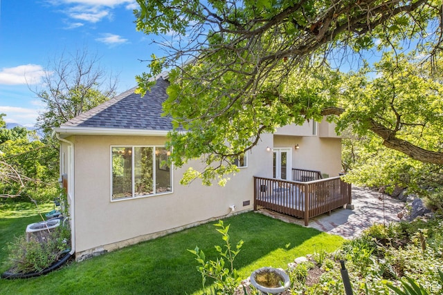 rear view of property with a deck, roof with shingles, a lawn, stucco siding, and french doors