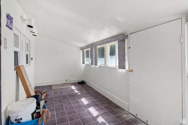 empty room featuring a textured ceiling, dark tile patterned floors, and baseboards
