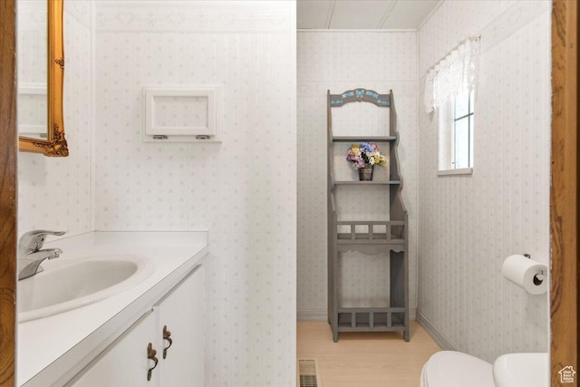 half bath featuring wood finished floors, toilet, ornamental molding, and vanity