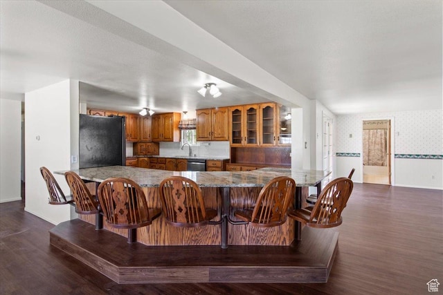 kitchen featuring freestanding refrigerator, brown cabinetry, wallpapered walls, dishwasher, and a peninsula