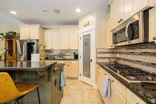 1608 W Boulder Creek Ln S, Layton, UT 84041 - kitchen with stainless steel appliances, a breakfast bar area, cream cabinets, backsplash, and dark stone countertops
