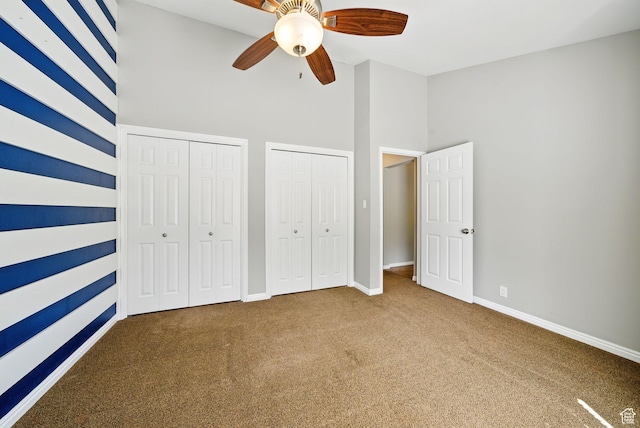unfurnished bedroom featuring multiple closets, carpet, baseboards, a high ceiling, and a ceiling fan
