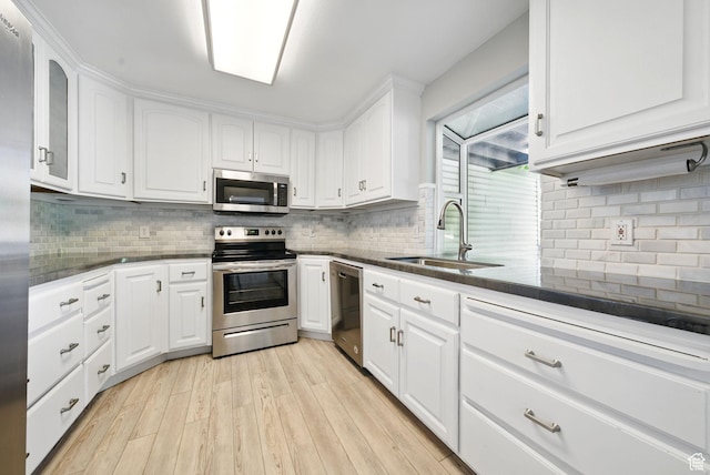 kitchen featuring stainless steel appliances, a sink, white cabinets, decorative backsplash, and light wood finished floors
