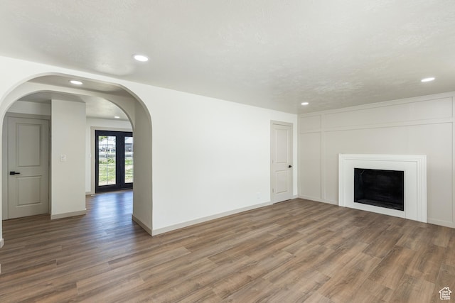 unfurnished living room with recessed lighting, wood finished floors, a fireplace, baseboards, and arched walkways