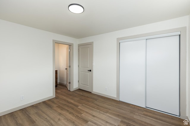 unfurnished bedroom featuring wood finished floors, baseboards, and a closet