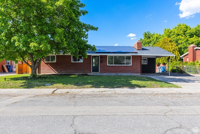 view of front facade featuring brick siding, driveway, roof mounted solar panels, a carport, and a chimney