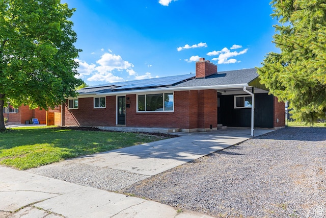 ranch-style house with driveway, a chimney, a front yard, brick siding, and solar panels