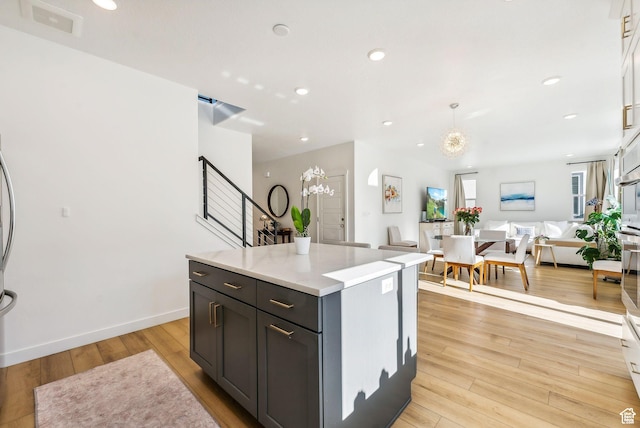 kitchen with open floor plan, light wood-type flooring, light countertops, a center island, and a chandelier