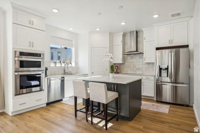 kitchen with stainless steel appliances, wall chimney exhaust hood, a sink, white cabinetry, and recessed lighting