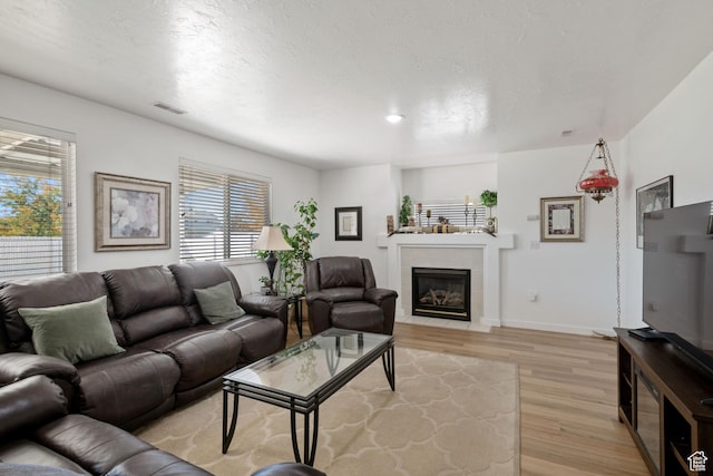 living room with light wood finished floors, a tiled fireplace, and baseboards