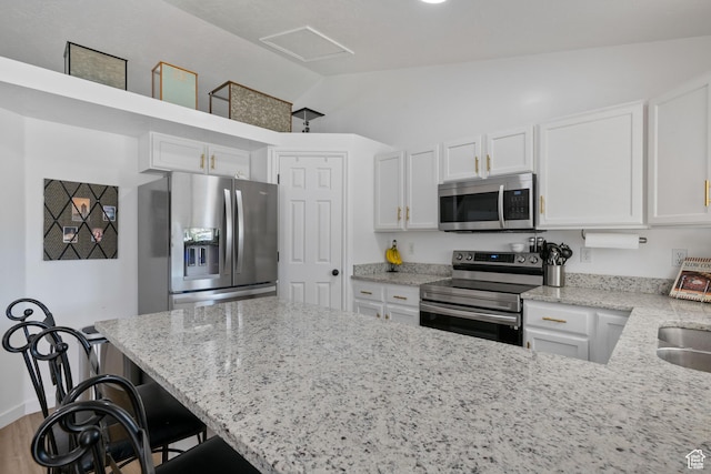 kitchen featuring appliances with stainless steel finishes, white cabinetry, light stone countertops, and lofted ceiling