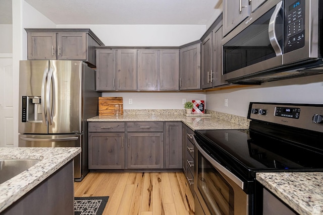466 W 1595 N Unit 45-103, Logan, UT 84341 - kitchen featuring appliances with stainless steel finishes, light wood-style flooring, dark brown cabinetry, and light stone countertops