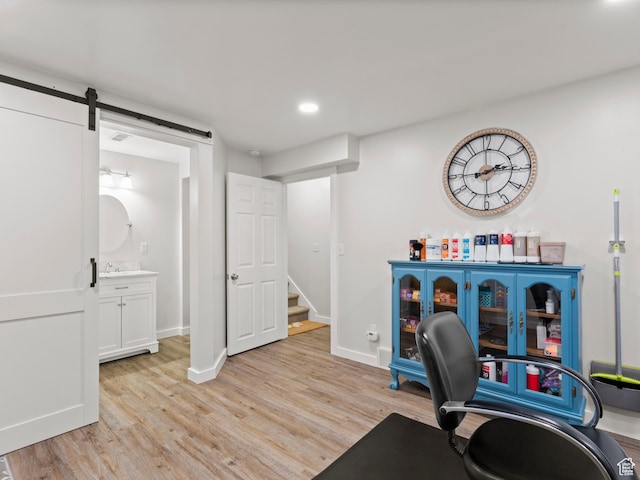 home office with light wood-style flooring, baseboards, a barn door, recessed lighting, and a sink