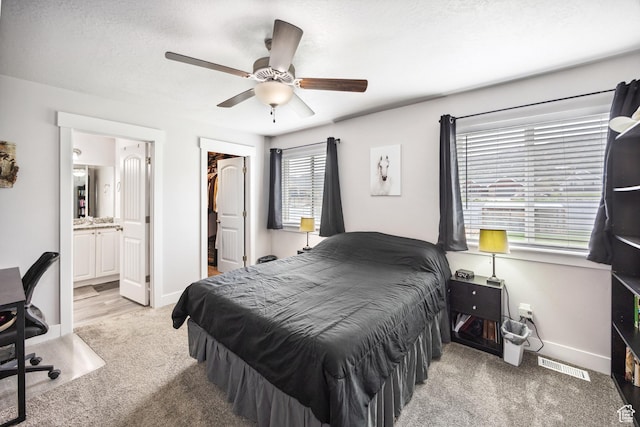 bedroom featuring light carpet, ensuite bathroom, ceiling fan, a spacious closet, and baseboards