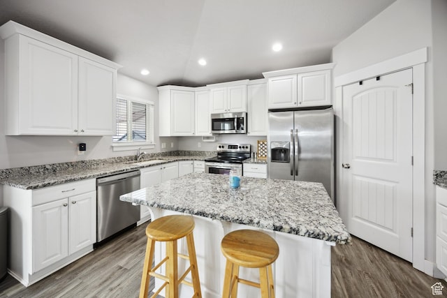 kitchen with stainless steel appliances, a sink, wood finished floors, a center island, and white cabinets
