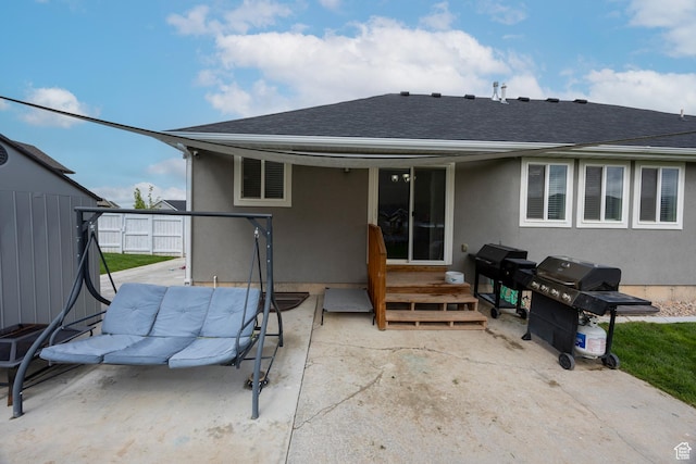 back of property with a shingled roof, stucco siding, and a patio