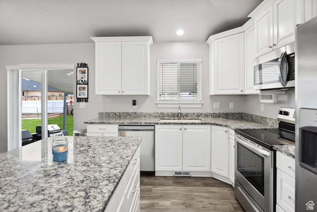 kitchen with appliances with stainless steel finishes, a sink, wood finished floors, white cabinets, and plenty of natural light
