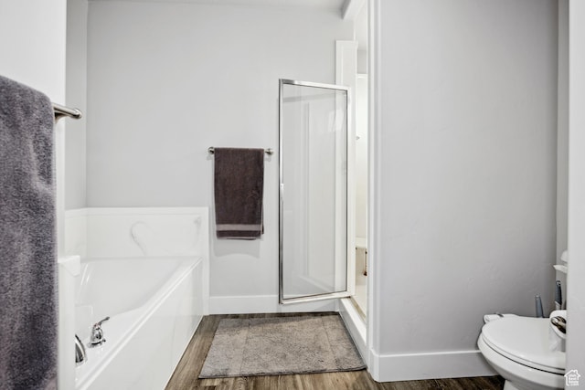 bathroom featuring wood finished floors, toilet, baseboards, a shower stall, and a garden tub