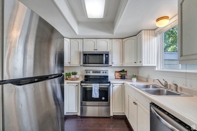 kitchen featuring appliances with stainless steel finishes, a sink, light countertops, and a tray ceiling