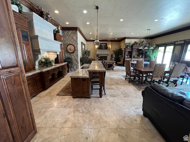 kitchen with open floor plan, a fireplace, ornamental molding, a kitchen bar, and light stone counters